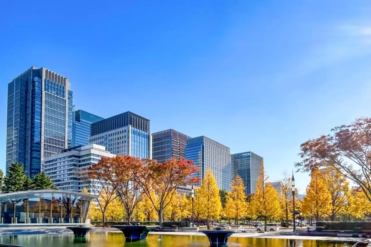公園の先にそびえる高層ビルと紅葉した木々